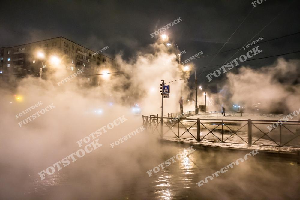 На фотографии изображен перекресток в Санкт-Петербурге, окутанный клубами пара, вероятно, из-за теплотрассы. Яркие огни уличных фонарей пробиваются сквозь густой пар, придавая сцене загадочность и неоновую атмосферу. Ночная тишина и отсутствие людей на фоне жилых домов усиливают ощущение уединенности и мистики, типичное для зимних ночей в городе.